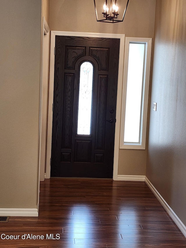 entryway with dark wood-type flooring, plenty of natural light, and a chandelier