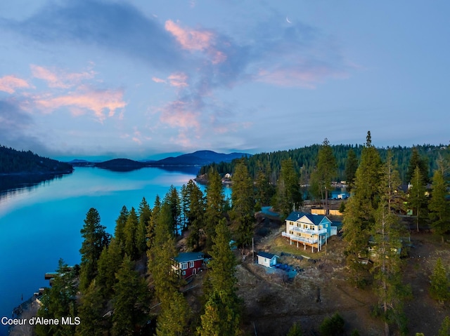 aerial view at dusk with a water view and a wooded view