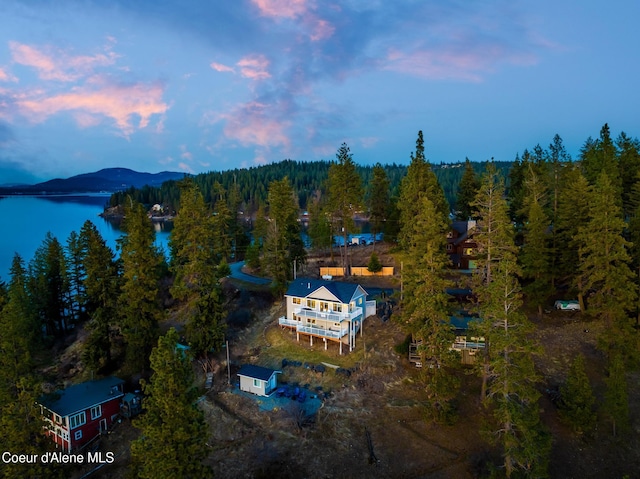 aerial view at dusk featuring a forest view and a water view