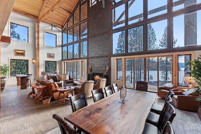 dining space featuring ceiling fan, a large fireplace, a water view, wood ceiling, and beamed ceiling