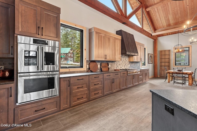 kitchen with custom exhaust hood, stainless steel appliances, dark countertops, hanging light fixtures, and decorative backsplash