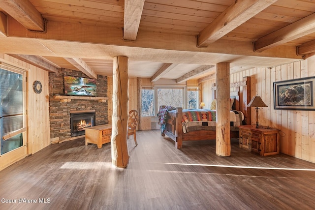 bedroom with dark wood finished floors, wood walls, a stone fireplace, wooden ceiling, and beamed ceiling