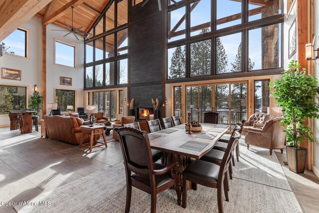 dining space with a large fireplace, a ceiling fan, wooden ceiling, beamed ceiling, and a high ceiling