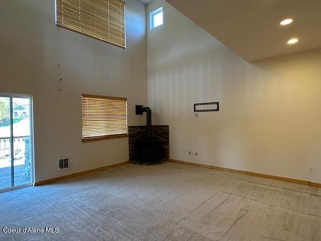 carpeted empty room featuring a wood stove, a high ceiling, and plenty of natural light