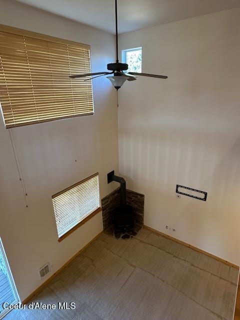 unfurnished living room with ceiling fan and a wood stove