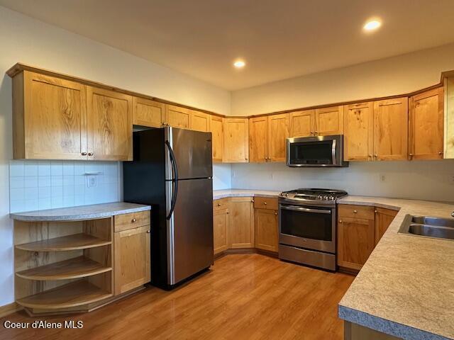 kitchen with sink, backsplash, light wood-type flooring, and stainless steel appliances