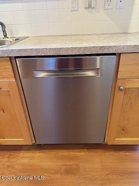 interior details with sink, stainless steel dishwasher, decorative backsplash, and light hardwood / wood-style floors