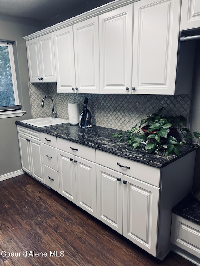 kitchen with sink, white cabinetry, dark stone countertops, dark hardwood / wood-style floors, and backsplash