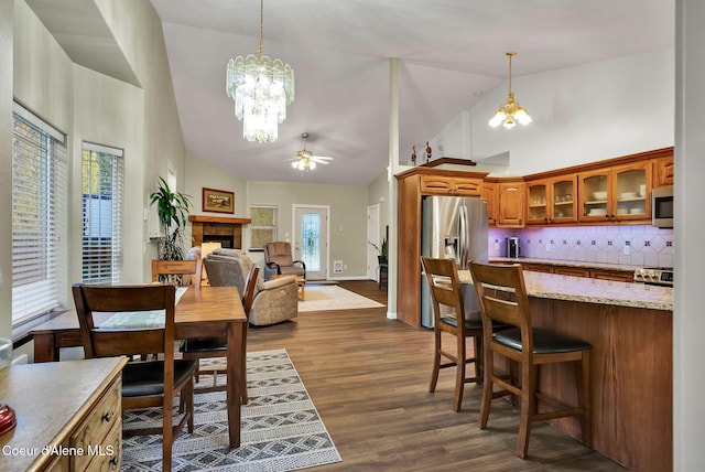 dining space with dark wood-type flooring, ceiling fan with notable chandelier, and high vaulted ceiling