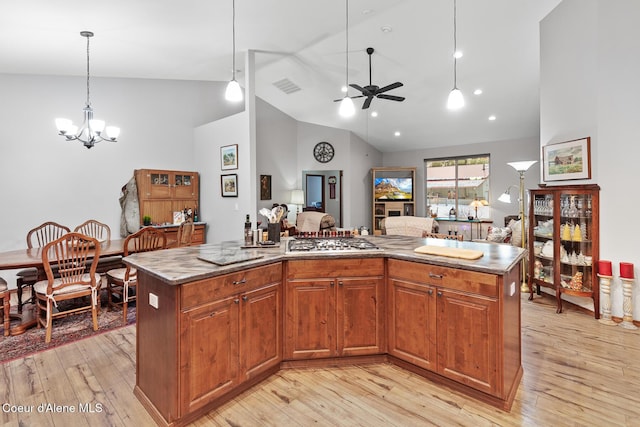 kitchen featuring stainless steel gas cooktop, light wood-style floors, open floor plan, ceiling fan with notable chandelier, and hanging light fixtures