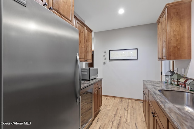 kitchen with appliances with stainless steel finishes, brown cabinets, light wood finished floors, and beverage cooler