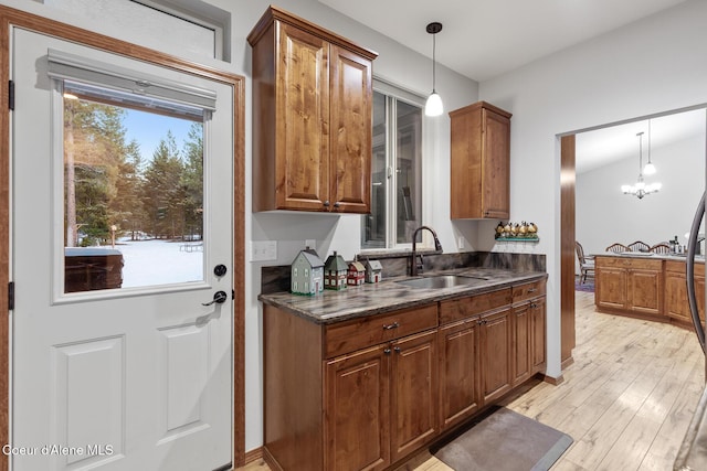kitchen with dark countertops, light wood-style floors, brown cabinets, a sink, and hanging light fixtures