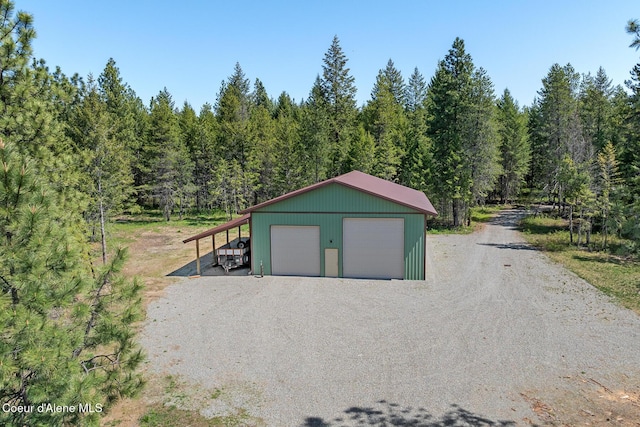 garage featuring a garage, gravel driveway, and a forest view