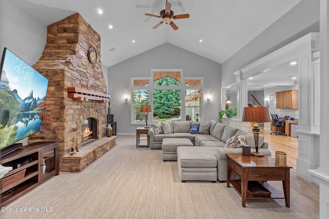 living room featuring ceiling fan, high vaulted ceiling, a stone fireplace, and ornate columns