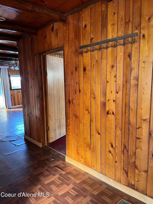 empty room with beam ceiling, dark parquet floors, and wood walls