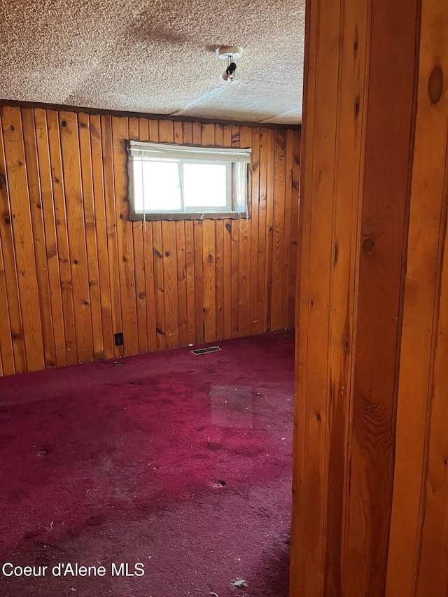 spare room with carpet floors, wooden walls, and a textured ceiling