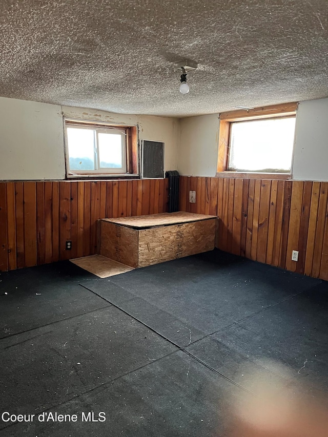 unfurnished room with plenty of natural light, a textured ceiling, and wood walls