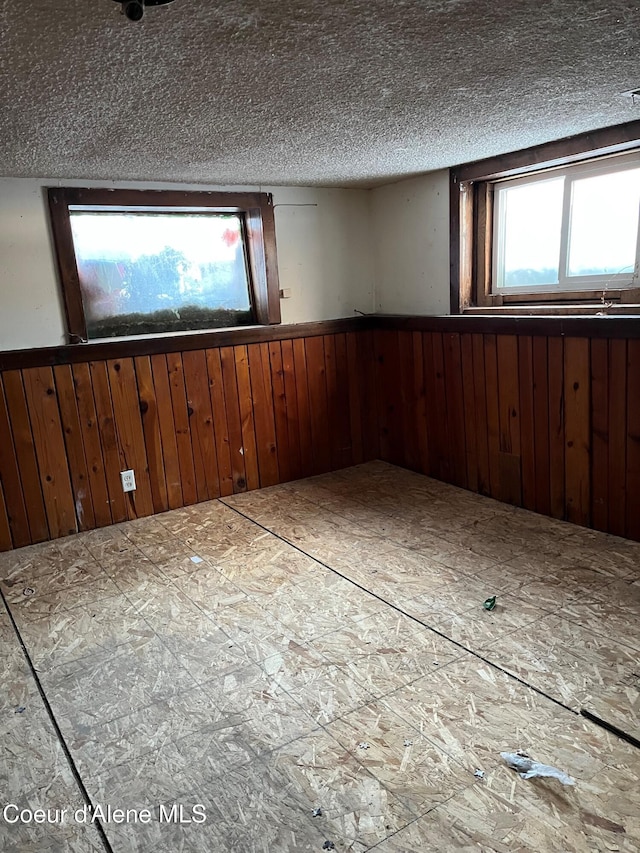 empty room with a healthy amount of sunlight, a textured ceiling, and wooden walls