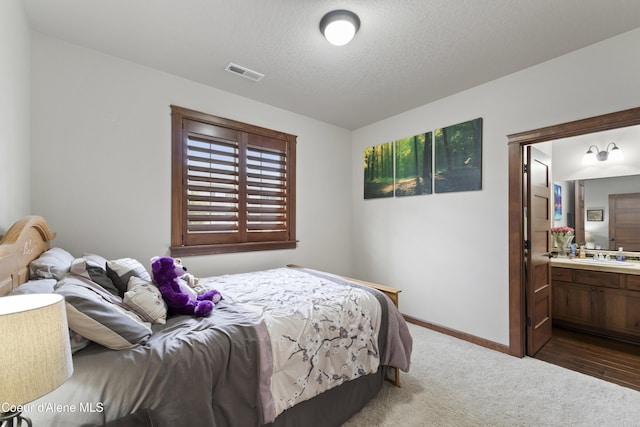 carpeted bedroom featuring connected bathroom, sink, and a textured ceiling