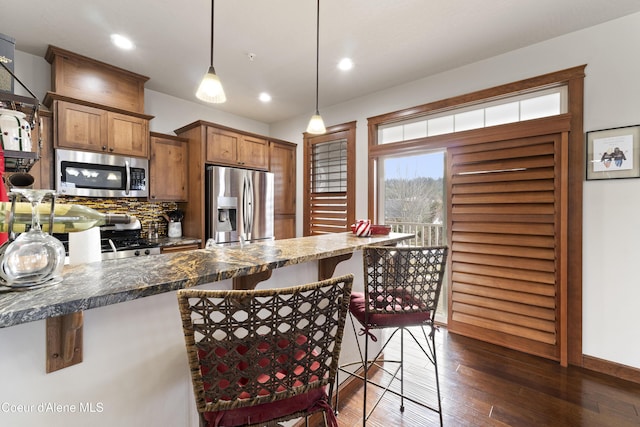 kitchen with appliances with stainless steel finishes, dark hardwood / wood-style floors, tasteful backsplash, a kitchen bar, and hanging light fixtures