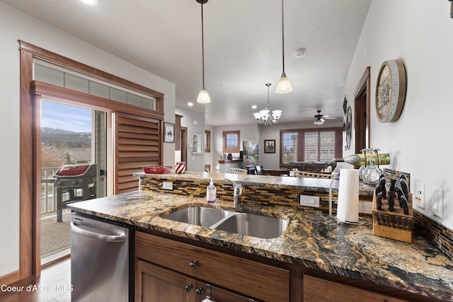 kitchen featuring sink, ceiling fan with notable chandelier, dishwasher, decorative light fixtures, and dark stone counters