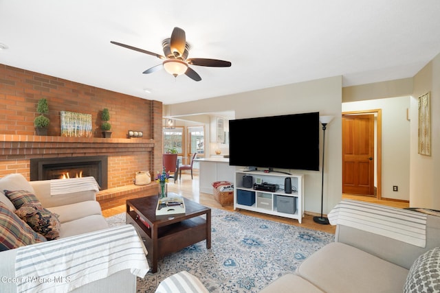 living room with ceiling fan, a brick fireplace, and light wood-type flooring