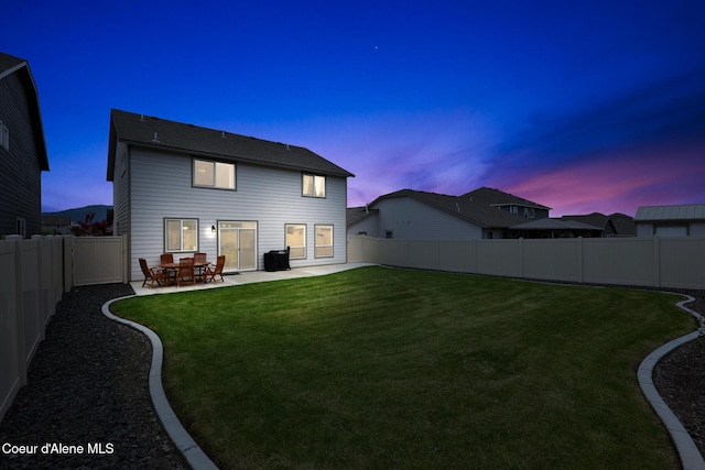 back house at dusk with a patio area and a lawn