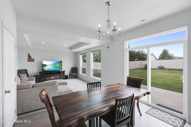 dining room with a notable chandelier, a wealth of natural light, and a raised ceiling