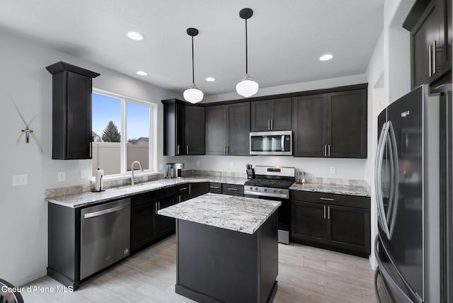 kitchen featuring stainless steel appliances, decorative light fixtures, a center island, and light hardwood / wood-style flooring