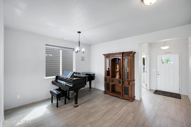 miscellaneous room featuring a notable chandelier, a textured ceiling, and light wood-type flooring