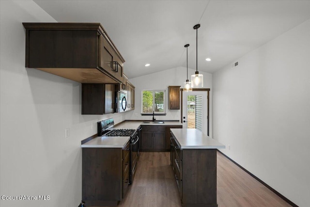 kitchen featuring a kitchen island, black gas range oven, sink, hanging light fixtures, and light hardwood / wood-style floors