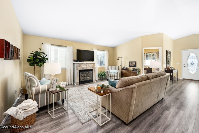 living room with vaulted ceiling, a tiled fireplace, and hardwood / wood-style floors