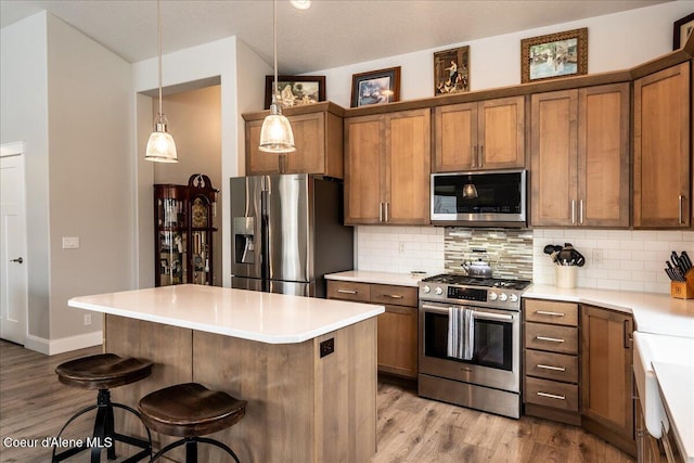 kitchen featuring a breakfast bar, tasteful backsplash, hanging light fixtures, light hardwood / wood-style floors, and stainless steel appliances