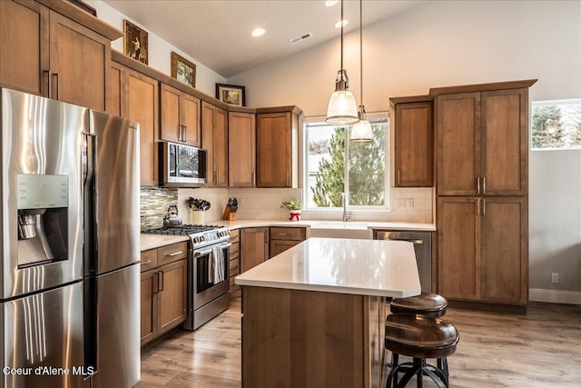 kitchen featuring decorative light fixtures, a center island, vaulted ceiling, stainless steel appliances, and light hardwood / wood-style floors