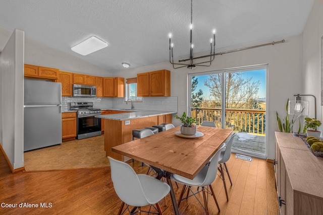 dining space with sink, a chandelier, vaulted ceiling, a textured ceiling, and light wood-type flooring