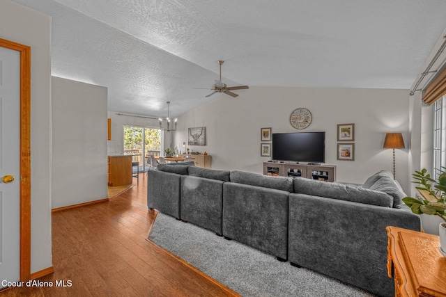 living room featuring ceiling fan with notable chandelier, vaulted ceiling, light hardwood / wood-style flooring, and a textured ceiling