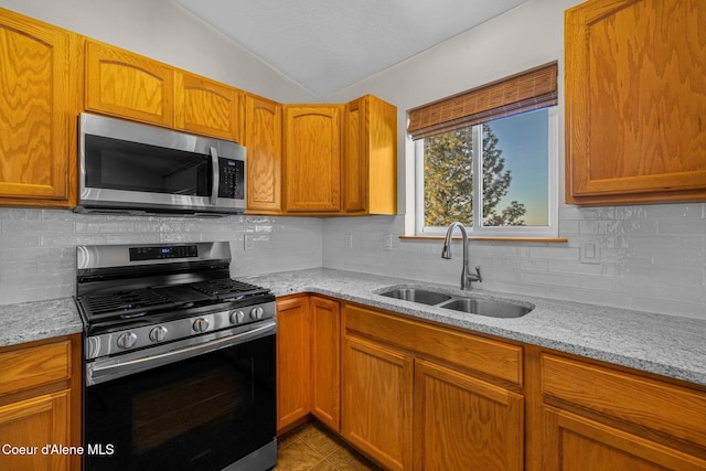 kitchen featuring lofted ceiling, sink, stainless steel appliances, tasteful backsplash, and light stone countertops