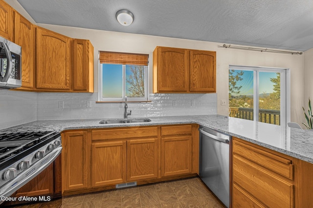 kitchen with sink, a textured ceiling, stainless steel appliances, light stone countertops, and backsplash