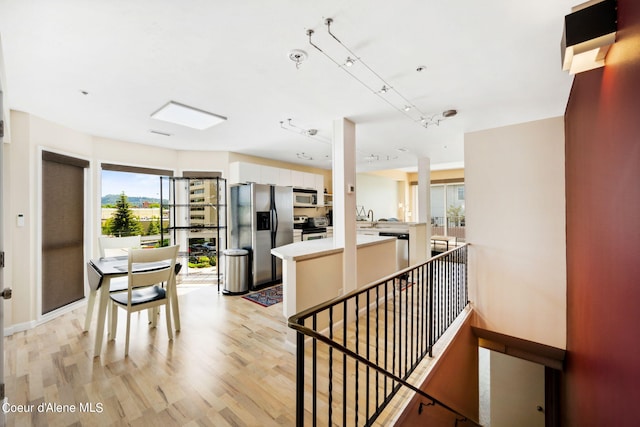 interior space featuring rail lighting, appliances with stainless steel finishes, white cabinetry, kitchen peninsula, and light wood-type flooring