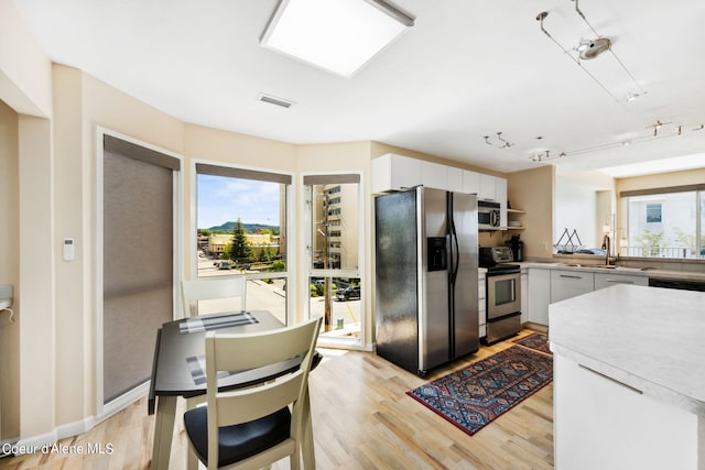 kitchen featuring rail lighting, sink, white cabinets, light hardwood / wood-style floors, and stainless steel appliances