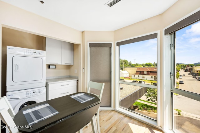 washroom featuring stacked washer and dryer, light hardwood / wood-style flooring, and cabinets