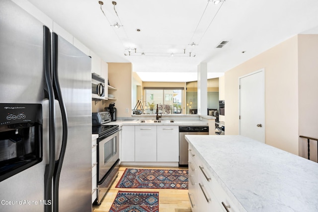 kitchen featuring rail lighting, sink, white cabinetry, light hardwood / wood-style flooring, and appliances with stainless steel finishes