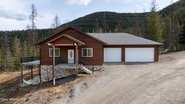 view of front of property featuring a mountain view, a wooded view, driveway, and roof with shingles