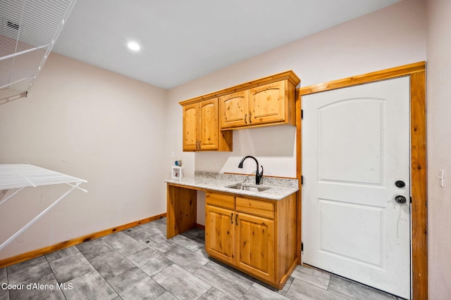 kitchen featuring light stone counters, baseboards, and a sink