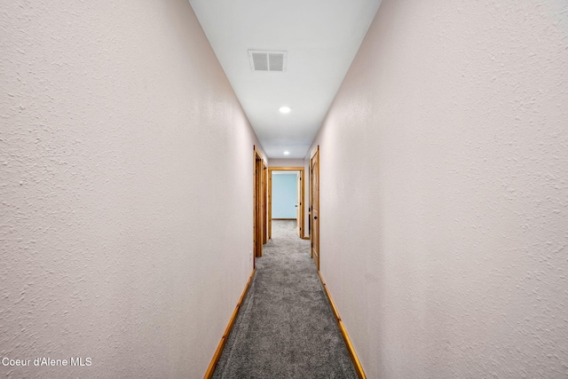 hallway with visible vents, carpet flooring, and a textured wall