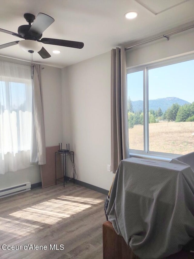 interior space featuring hardwood / wood-style flooring, a mountain view, a baseboard heating unit, and ceiling fan