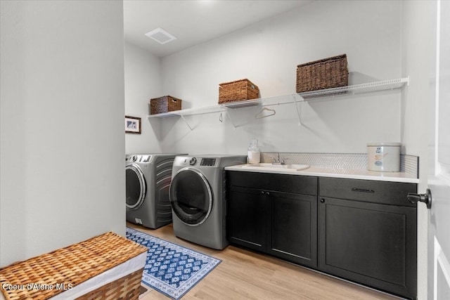 clothes washing area with cabinets, sink, washing machine and dryer, and light hardwood / wood-style flooring