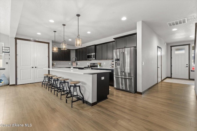 kitchen with a kitchen bar, hanging light fixtures, an island with sink, stainless steel appliances, and hardwood / wood-style floors