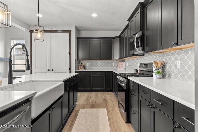 kitchen with sink, decorative light fixtures, appliances with stainless steel finishes, light hardwood / wood-style floors, and decorative backsplash