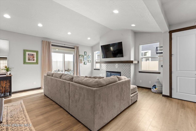 living room featuring vaulted ceiling, a textured ceiling, a fireplace, and light hardwood / wood-style floors